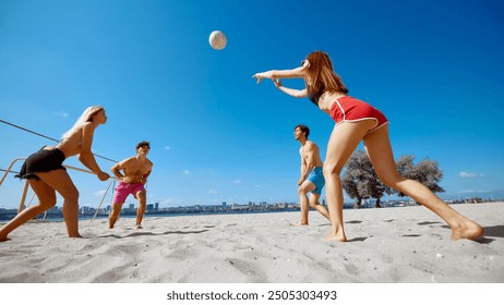 Young people, friends, men and women competing in a high-energy game of beach volleyball, under clear blue sky. Concept of sport, summer activity, leisure games, friendship - Powered by Shutterstock