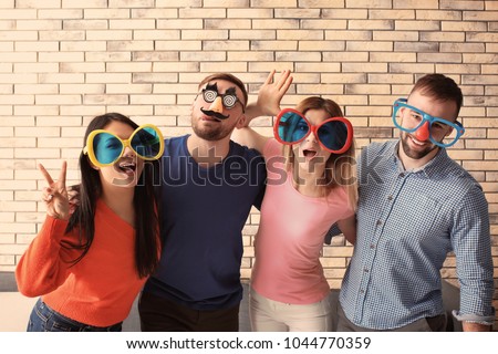 Young people in funny disguise posing on brick wall background. April fool's day celebration