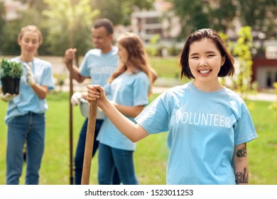 Young people girls and boy volunteers outdoors helping nature planting trees asian girl close-up standing holding shovel looking camera smiling cheerful blurred background - Powered by Shutterstock