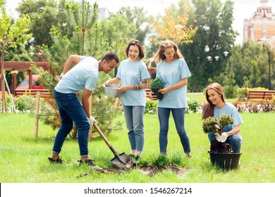 Young people girls and boy volunteers outdoors helping nature planting trees together digging grouns smiling cheerful
