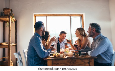 Young People Got Together By Table With Delicious Food And Glasses Of Red Wine To Celebrate A Special Occasion. Group Of Friends Enjoying Dinner Party.