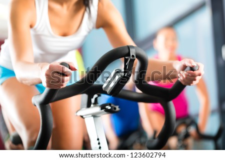 Young People - group of women and men - doing sport biking in the gym for fitness