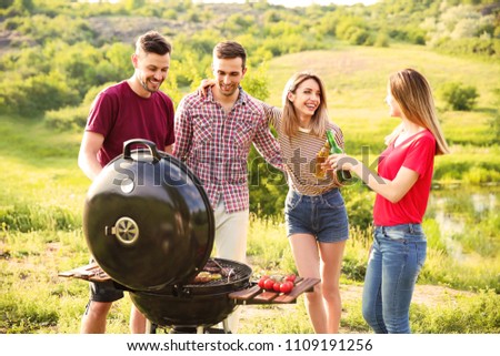 Young people having barbecue in wilderness. Camping season