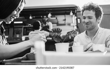 Young people having fun eating at food truck restaurant outdoor - Focus on man face - Black and white editing - Powered by Shutterstock