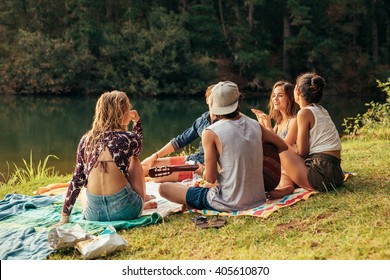 Young People Having Picnic Near A Lake. Young Friends Relaxing By A Lake.