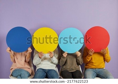 Young people hide their faces behind round colorful blue, yellow and red speech bubble banners that they are holding. Group of unrecognizable men and women trying to express their opinions anonymously