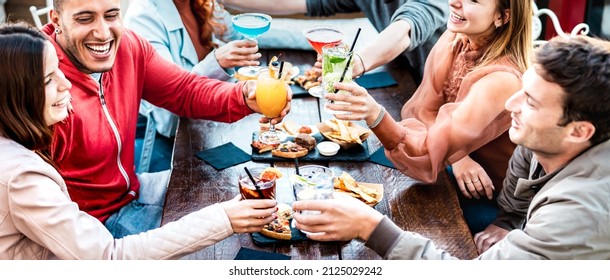 Young people holding multicolored drinks - Trendy fashion friends having fun together toasting cocktails at happy hour - Social gathering life style concept on vivid filter with focus on mid glasses - Powered by Shutterstock