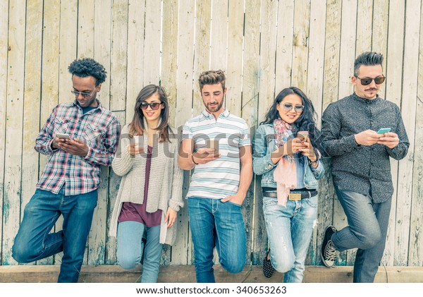 Young people looking down at\
cellular phone - Teenagers leaning on a wall and texting with their\
smartphones - Concepts about technology and global\
communication