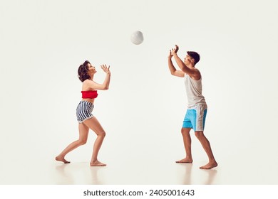 Jóvenes, hombres y mujeres, amigos jugando al voleibol playa, divirtiéndose en la ciudad costera con un fondo blanco. Concepto de vacaciones de verano, viajes, estilo retro, moda, ocio