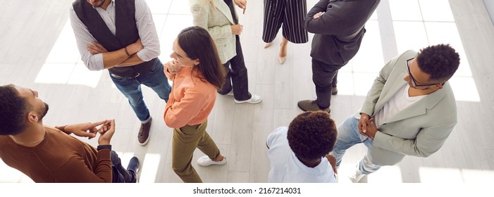 Young people meeting, interacting and making contacts at business event session. Group of multi ethnic participants standing in office and talking. High angle, overhead top view, above. Header, banner