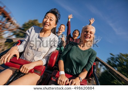 Young people on a thrilling roller coaster ride. Group of friends having fun at amusement park.