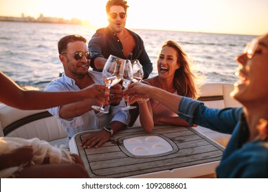 Young people on yacht drinking together. Group of friends toasting drinks and having party on boat.