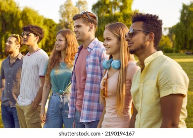 Young people at an outdoor summer festival. Diverse audience enjoying a show in nature. Company of several happy male and female friends standing in the park and watching a live open-air performance