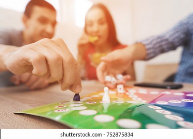 Young People Play A Board Game Using A Dice And Chips. On The Table They Have Glasses With Alcoholic Drinks. They Have Fun Playing A Game.