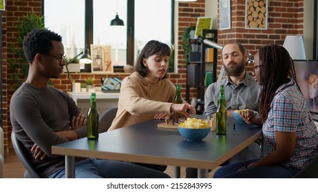 Young People Playing Board Games Together In Apartment, Enjoying Free Time Activity To Have Fun With Chess Match. Multiethnic Group Of Friends Laughing With Strategy Play, Entertainment Concept.