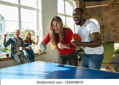 Young people playing table tennis in workplace, having fun. Friends in casual clothes play ping pong together at sunny day. Concept of leisure activity, sport, friendship, teambuilding, teamwork.