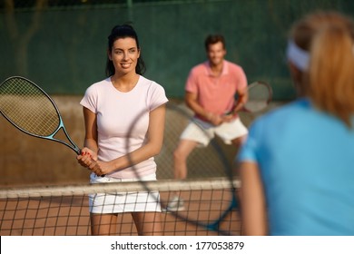 Young people playing tennis, mixed doubles, smiling.