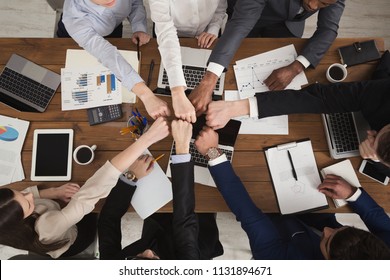 Young people putting their fists together as symbol of unity and achievement, top view. Group of people fist bump assemble together over workplace. Teamwork concept, copy space in middle