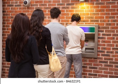 Young People Queuing To Withdraw Cash In An ATM