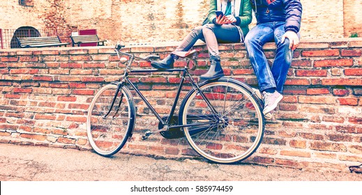 Young People With Retro Bike Sitting On Old Urban Wall Typing Message On Phone At Winter Time - Couple Of Best Friends Hanging Around Using Mobile Cropped Image Vintage Filter Look Enhanced Red Tones