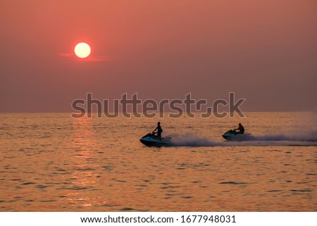 Young people ride a scooter on the sea at sunset