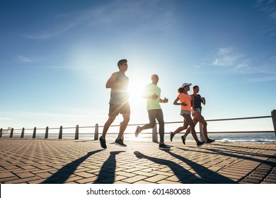 Young people running along a seaside promenade. Runners training outdoors by the seaside on a sunny day. - Powered by Shutterstock