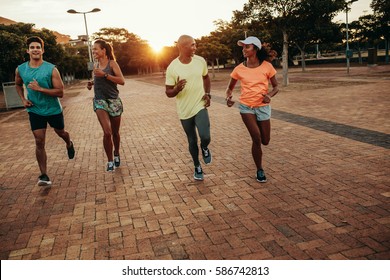 Young People Running Together At The Park. Runners Training Outdoors In Evening.