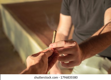 Young people sharing a marijuana joint during a sunset on the street.