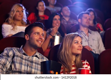 Young people sitting at auditorium of movie theater, watching movie.