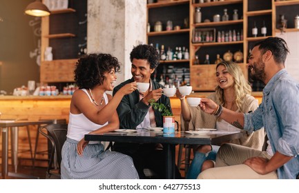 Young People Sitting At Cafe Table And Having Coffee Together. Group Of Friends Making A Toast With Coffee.