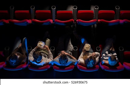 Young people sitting at the cinema, watching a movie and eating pop corn, top view