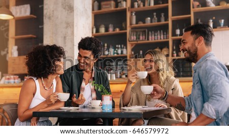 Young people sitting at a coffee shop and talking. Group of friends having coffee together in a cafe.