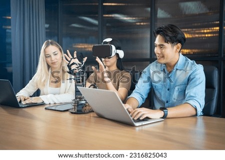 Young people sitting at a desk wearing VR glasses while trying out a robotic arm project. Group of multiethnic students studying together in the library