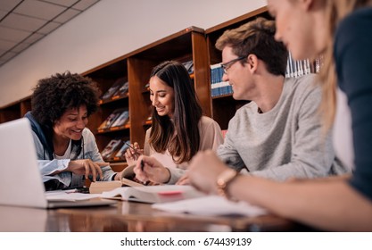 Young People Sitting At Table Reading Reference Books For Study Notes. Group Of Young Students Doing Assignment In Library.