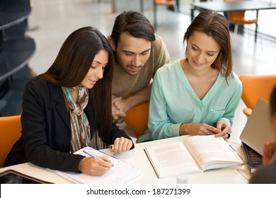 Young People Sitting At Table Working On School Project In Library.  University Students Taking Reference From Books For Study.