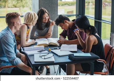 Young People Sitting At Table Working On School Assignment. Multiracial Group Of Students Studying Together In A Library.