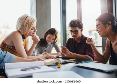 Young People Sitting Together At Table Working On School Assignment. Diverse Group Of Students Studying In A Library.