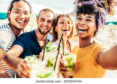 Young people toasting mojito drinks at beach cocktail bar - Happy multiracial friends having fun taking selfie portrait enjoying summer holidays - Youth, beverage and summertime concept - Powered by Shutterstock