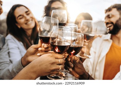 Jóvenes tostando vasos de vino tinto en la casa de campo en el campo de los viñedos - Amigos felices disfrutando de la hora feliz en el bar restaurante de la bodega - Concepto de estilo de vida con chicos y chicas comiendo en la cena
