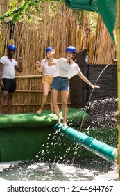 Young People Try To Walk The Wet Log In The Theme Park. High Quality Photo