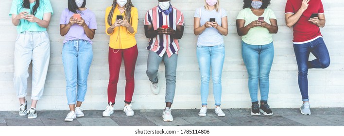 Young people wearing face safety masks using mobile phones while keeping social distance during coronavirus time - Technology and covid-19 spread prevention concept - Main focus on left girls hands