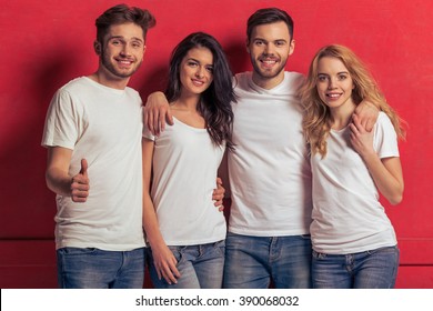 Young People In White T Shirts And Jeans Are Looking At Camera And Smiling, Standing Against Red Background