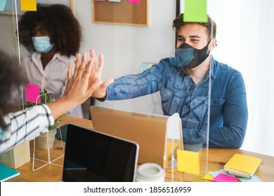 Young People Working Inside A Coworking Behind Safety Plexiglass During Coronavirus Outbreak - Social Distance Concept - Focus On Man Face