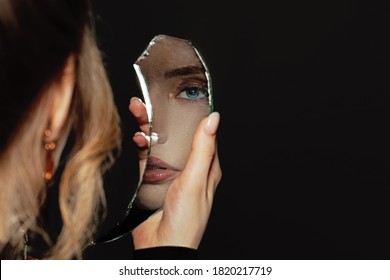 Young perfect woman holding broken self-image mirror on black background