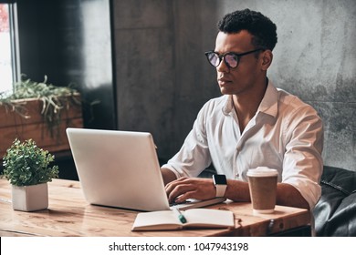 Young Perfectionist. Handsome Young African Man In Eyewear Working Using Laptop While Sitting In The Office