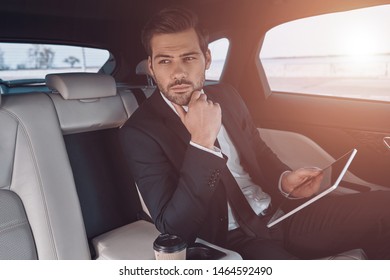 Young Perfectionist. Handsome Young Man In Full Suit Working Using Digital Tablet While Sitting In The Car