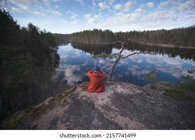 A young person on the shore of a mirror picturesque forest lake. A man photographs a picturesque landscape. Back view
