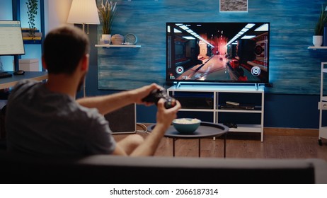 Young person playing with modern technology gadget using video games console on television. Caucasian gamer with wireless controller sitting at home having fun with digital action