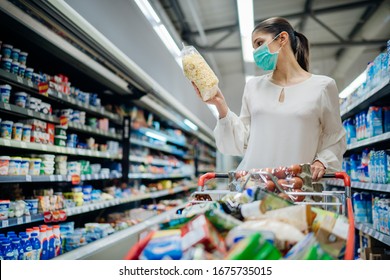 Young Person With Protective Face Mask Buying Groceries/supplies In The Supermarket.Preparation For A Pandemic Quarantine Due To Coronavirus Covid-19 Outbreak.Choosing Nonperishable Food Essentials