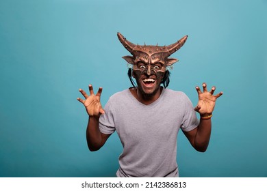 Young Person Wearing Traditional Indigenous Face Mask Used In Shaman Culture And History To Create Native Tribal Ritual. Man Using Traditional Tribe Art And Cultural Object For Entertainment.